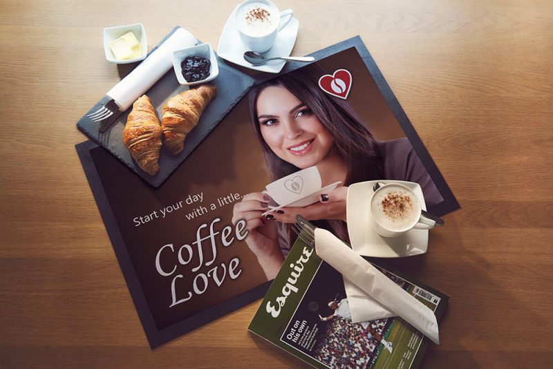 Promotional matting for a coffee shop on a table with coffee and food on a plate